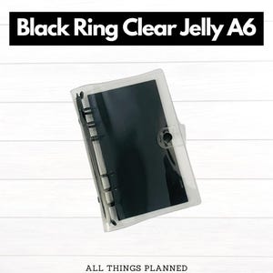 May include: A clear jelly A6 ring binder with a black ring mechanism and a black interior. The binder is transparent, allowing the contents to be visible. The text "Black Ring Clear Jelly A6" is displayed at the top.
