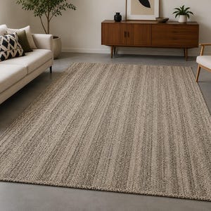 May include: A large rectangular rug in neutral tones. The rug features a woven texture with vertical stripes in beige and grey. It is placed on a concrete floor, complementing the room's decor. The rug's dimensions are suitable for a living room.