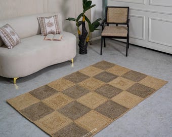 Puede incluir: Una alfombra rectangular de yute con un patrón de tablero de ajedrez de cuadrados marrones claros y marrones oscuros alternados. La alfombra está colocada sobre un suelo gris en una habitación con un sofá blanco, cojines y una silla negra.