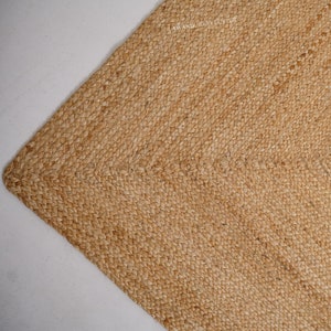 May include: A natural fibre rug made of woven jute, with a light brown colour and a textured surface. The rug has a subtle sheen and a slightly rough texture.