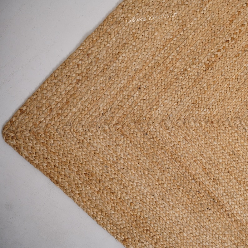 Puede incluir: Una alfombra de fibra natural hecha de yute tejido, de color marr&oacute;n claro y superficie texturizada. La alfombra tiene un brillo sutil y una textura ligeramente rugosa.