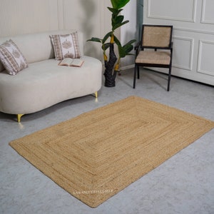 Puede incluir: Una alfombra rectangular de fibra natural de color marr&oacute;n claro. La alfombra est&aacute; hecha de yute tejido y tiene una superficie ligeramente texturizada. La alfombra est&aacute; colocada sobre un suelo gris claro en un sal&oacute;n.