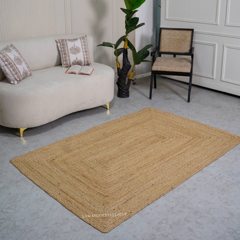 Puede incluir: Una alfombra rectangular de fibra natural de color marr&oacute;n claro. La alfombra est&aacute; hecha de yute tejido y tiene una superficie ligeramente texturizada. La alfombra est&aacute; colocada sobre un suelo gris claro en un sal&oacute;n.