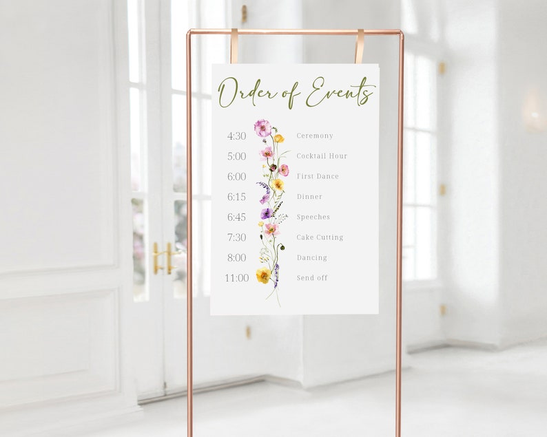 May include: A white sign with a floral design and the text "Order of Events" with a list of wedding events and times. The sign is on a gold stand.