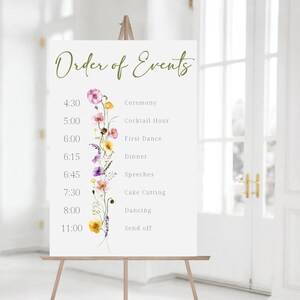 May include: A white sign with a floral design and the text "Order of Events" with a list of events and times for a wedding reception.