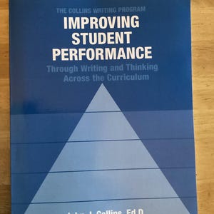 May include: A blue book with the title "IMPROVING STUDENT PERFORMANCE" by John J. Collins, Ed.D. The cover features white text and a light blue pyramid graphic. It's part of "THE COLLINS WRITING PROGRAM", focusing on writing and thinking across the curriculum.