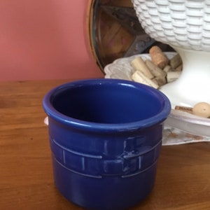 May include: A blue ceramic crock with a woven pattern. The crock is empty and sitting on a wooden surface.