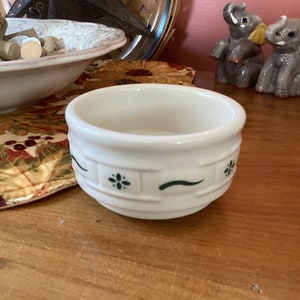 May include: A small white ceramic bowl with a green and white floral design. The bowl is sitting on a wooden table.