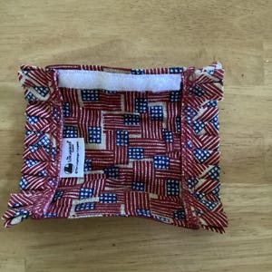 Könnte beinhalten: Ein rechteckiger Stoffeinsatz mit einem rot-weiß-blauen US-Flaggenmuster und gerüschten Kanten. Das Stück enthält einen weißen Klettverschluss am oberen Rand sowie ein weißes Etikett mit der Aufschrift The Longaberger Company.