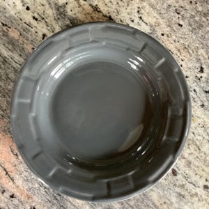 May include: A gray ceramic plate with a slightly raised, textured rim. The plate has a smooth, glossy interior and a simple, elegant design. The plate is suitable for serving various dishes.