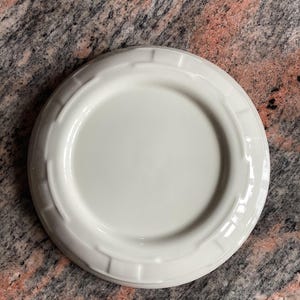 May include: A white ceramic plate with a raised rim and a scalloped edge. The plate is plain and has no design.