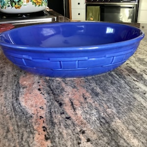 Puede incluir: Un cuenco grande, ovalado, de cerámica azul cobalto. El cuenco presenta un diseño texturizado, similar a una cesta, alrededor del borde. El cuenco está sobre una encimera de granito.