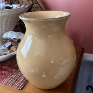 May include: A large, pale yellow ceramic vase with a light green rim. The vase has a rounded, bulbous shape and a smooth, glossy finish.