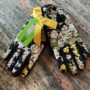 May include: A pair of black quilted gloves with a floral print in shades of yellow, green, and white. The gloves have a yellow bow tied around them.