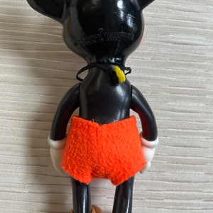 May include: Vintage Mickey Mouse figurine, viewed from the back, with black body and ears, orange shorts, and tan shoes. The figure has white gloves and a black collar with a yellow accent. The text "WALT DISNEY PRODUCTION MADE IN JAPAN" is visible.