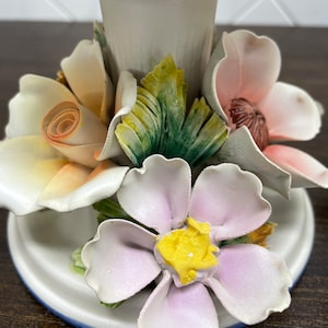 May include: A white ceramic pedestal with a floral design. The pedestal is decorated with pink, yellow, and green flowers. The flowers are three-dimensional and have a realistic appearance.