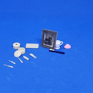 May include: A collection of miniature antique items against a blue backdrop. The items include a framed black and white photograph, a small white jug, a pink item, and various small, off-white accessories.