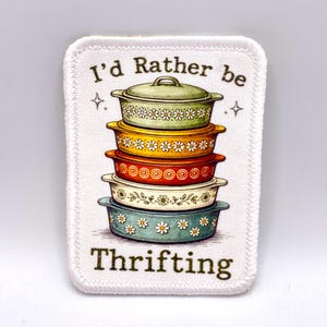 May include: A rectangular patch with a white border features a stack of colorful casserole dishes. The dishes are in shades of green, yellow, orange, white, and blue, decorated with floral patterns. Text reads "I'd Rather be Thrifting."