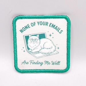 May include: Square patch with a teal border and white background. The patch features a white cat wearing glasses, lounging on a laptop. The text "NONE OF YOUR EMAILS" arches above the laptop, and "ARE FINDING ME WELL" is below.