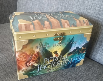 May include: A wooden treasure chest with a gold trim and a metal clasp. The chest is decorated with a blue and green image of a winged creature and the text "Percy Jackson" and "Rick Riordan".