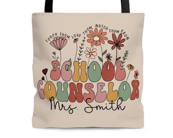 May include: Beige tote bag with black handles featuring the text "SCHOOL COUNSELOR Mrs. Smith" in colorful, retro-style lettering. The design includes floral elements and the phrases "Teach them, love them, watch them grow."