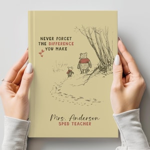 Könnte beinhalten: Ein hellgelbes Hardcover-Buch mit einer Strichzeichnung von Winnie Puuh und Ferkel, die an Bäumen vorbeigehen. Der Text lautet: NEVER FORGET THE DIFFERENCE YOU MAKE, Mrs. Anderson und SPED TEACHER, ergänzt durch drei kleine rote Herzen.