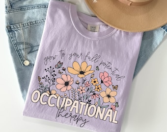 May include: A lavender t-shirt with a floral design and the text "grow to your full potential OCCUPATIONAL therapy".
