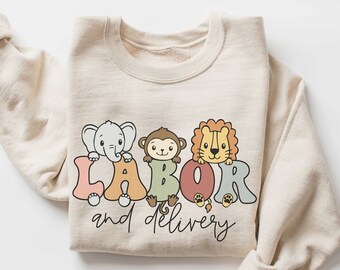 Op de afbeelding: Een beige sweatshirt met een afbeelding van dieren die letters vasthouden die "LABOR and DELIVERY" spellen. De dieren zijn een olifant, een aap en een leeuw.