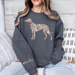Peut inclure: Un sweat-shirt gris fonc&eacute; avec un motif de chien floral. La silhouette du chien est remplie de fleurs et de feuillages roses, p&ecirc;che et cr&egrave;me. Le nom "Molly" est &eacute;crit sur la manche gauche en &eacute;criture cursive.