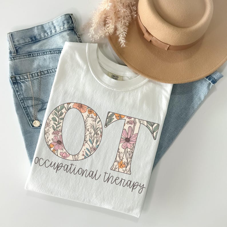 K&ouml;nnte beinhalten: Wei&szlig;es T-Shirt mit einem floralen Design, das "OT" f&uuml;r Ergotherapie buchstabiert.