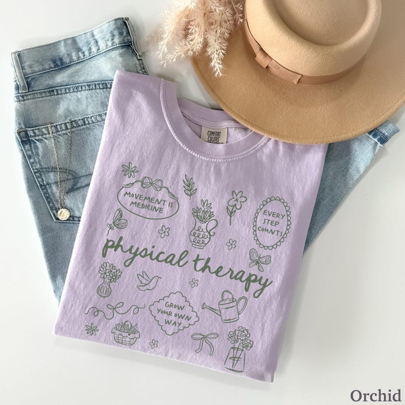 Puede incluir: Una camiseta lila con la frase "physical therapy" e ilustraciones verdes. La camiseta se combina con vaqueros azul claro, un sombrero beige y un collar plateado.