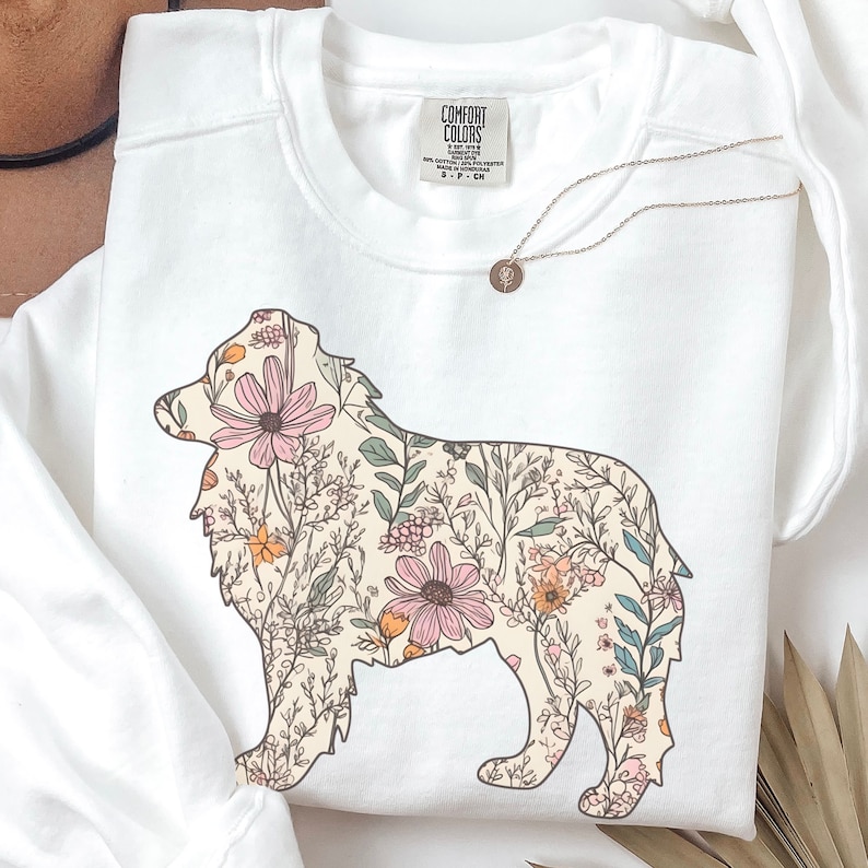 Pu&ograve; includere: Felpa bianca con una silhouette di pastore australiano con motivo floreale. Il cane &egrave; delineato in nero e riempito con una variet&agrave; di fiori rosa, arancioni e verdi.