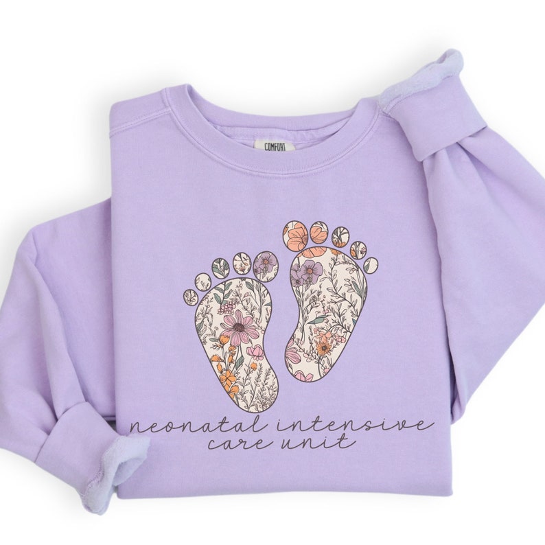 May include: A lavender sweatshirt with a floral design of two footprints and the text "neonatal intensive care unit".