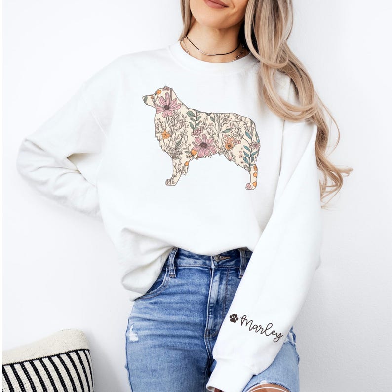 Puede incluir: Sudadera blanca con una silueta de perro con estampado floral. El perro es un pastor australiano. El texto "Marley" est&aacute; en la manga de la sudadera.