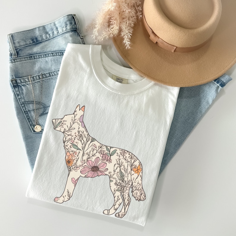 May include: White t-shirt with a floral design in the shape of a dog. The flowers are in shades of pink, orange, and green.