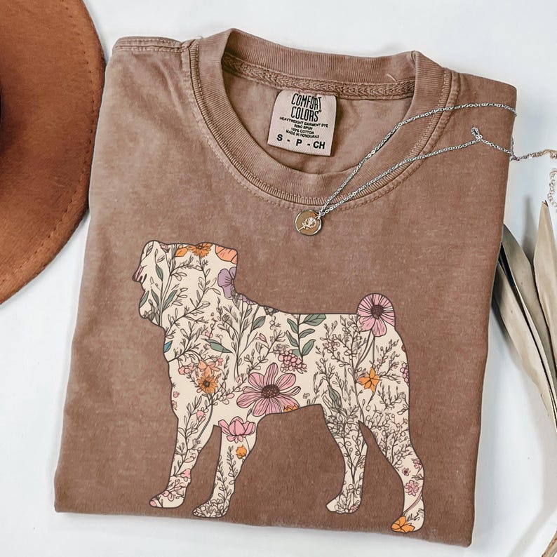 May include: A brown t-shirt with a floral print of a dog silhouette. The shirt has a distressed look and is made of a soft, comfortable fabric. The text "COMFORT COLORS" is visible on the tag.