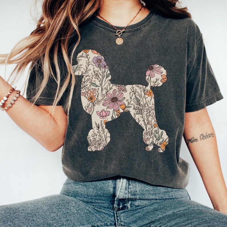 May include: A dark gray t-shirt with a floral poodle silhouette design. The flowers are in shades of pink, yellow, and orange.