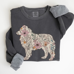Pu&ograve; includere: Una felpa grigia scura con un design floreale a forma di cane. I fiori sono rosa, arancioni e gialli.