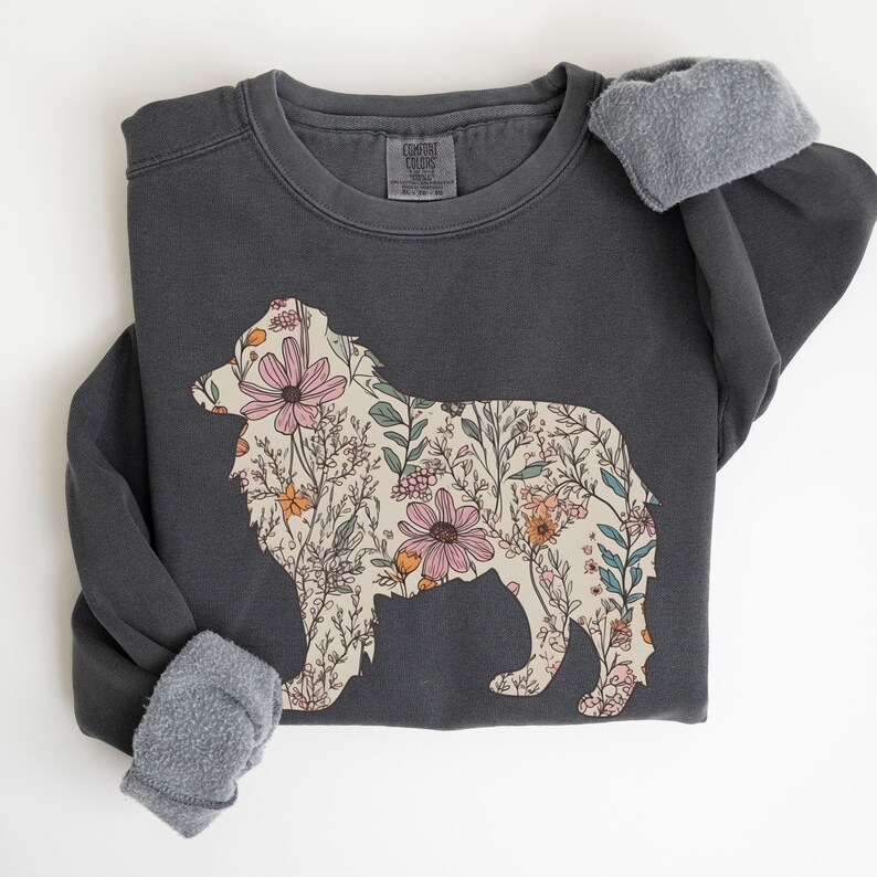Pu&ograve; includere: Una felpa grigia scura con un design floreale a forma di cane. I fiori sono rosa, arancioni e gialli.