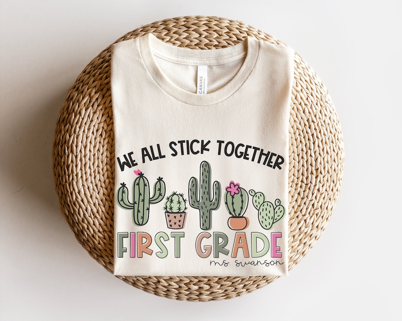May include: A beige t-shirt with the text "We all stick together first grade" and a row of cactus illustrations. The text "ms. swanson" is below the cactus illustrations.