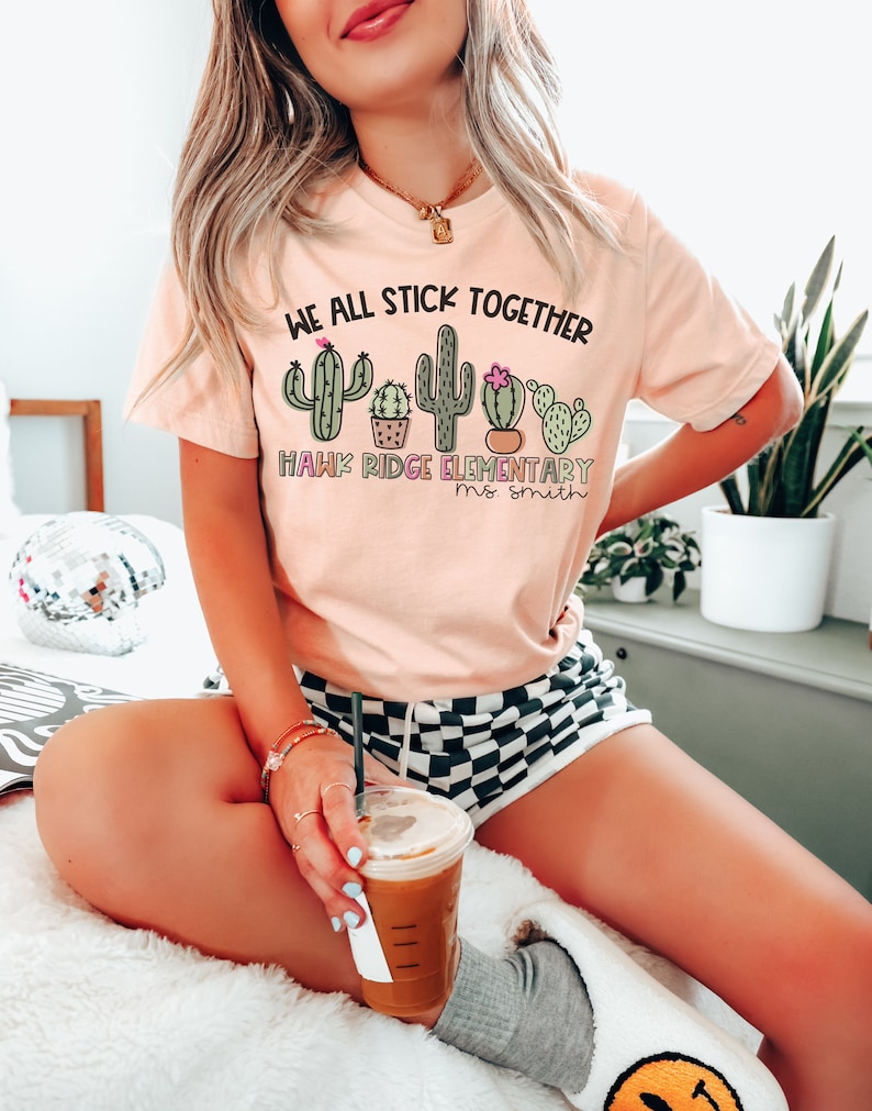 May include: A pink t-shirt with a cactus graphic and the text "We all stick together Hawk Ridge Elementary Ms. Smith".