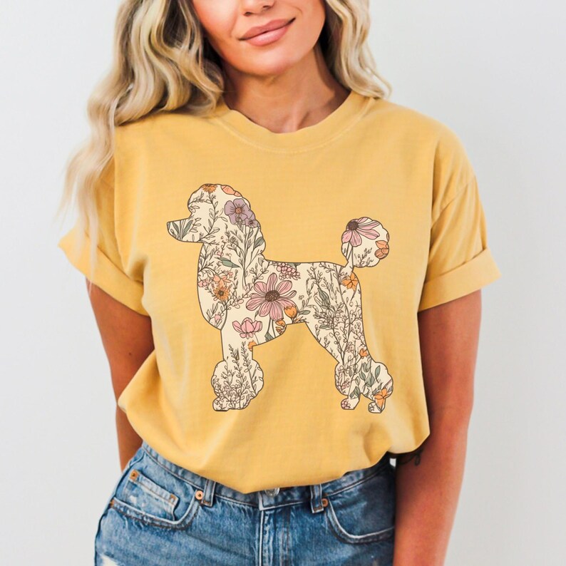 May include: A yellow t-shirt with a floral poodle silhouette design. The poodle is outlined in black and filled with a pattern of pink, purple, and yellow flowers.