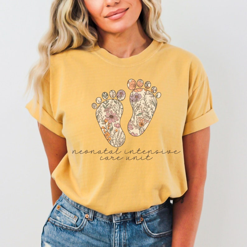 Puede incluir: Una camiseta amarilla con un dise&ntilde;o floral de dos huellas y el texto "neonatal intensive care unit".