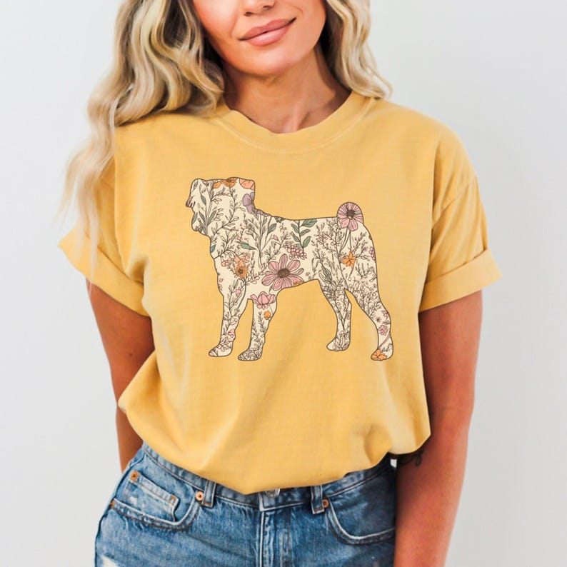 May include: A yellow t-shirt with a floral print of a dog silhouette. The flowers are in shades of pink, orange, and green.