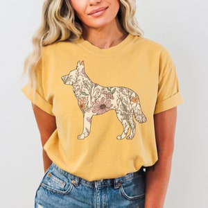 May include: A mustard yellow t-shirt with a floral print of a German Shepherd silhouette.