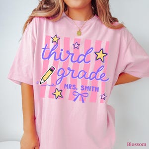 May include: Pink t-shirt with the words "third grade" in purple script, a yellow pencil graphic, and star and bow accents. The shirt also includes the text "MRS. SMITH".