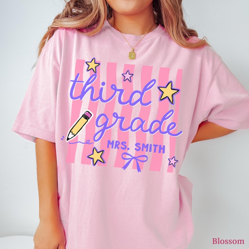 May include: Pink t-shirt with the words "third grade" in purple script, a yellow pencil graphic, and star and bow accents. The shirt also includes the text "MRS. SMITH".