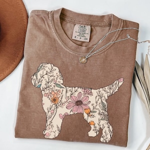 Könnte beinhalten: Ein braunes T-Shirt mit einem floralen Design eines Hundes. Das Shirt hat ein Etikett mit der Aufschrift "Comfort Colors" und "S - P - CH".