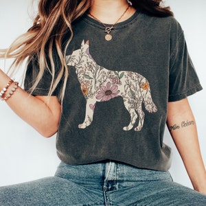 May include: A dark gray t-shirt with a floral design in the shape of a dog. The shirt has a crew neck and short sleeves. The model is wearing blue jeans.