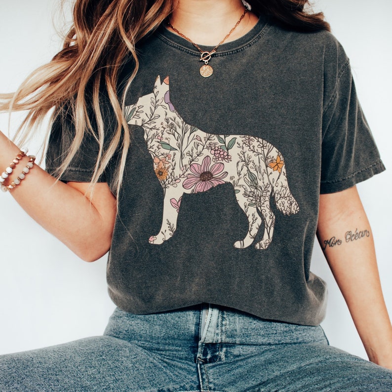 May include: A dark gray t-shirt with a floral design in the shape of a dog. The shirt has a crew neck and short sleeves. The model is wearing blue jeans.
